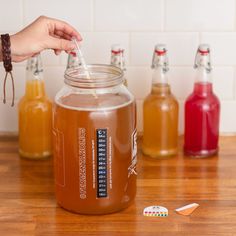 a person is holding a spoon in a mason jar filled with liquid next to several bottles