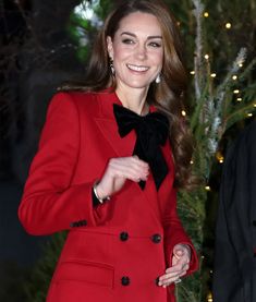 a woman in a red coat and black bow tie standing next to a christmas tree