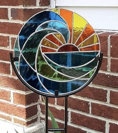 a colorful stained glass sundial sitting on top of a metal stand next to a brick wall