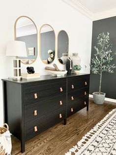 a black dresser with two mirrors and a potted plant on top in front of it