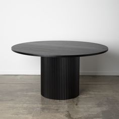 a black round table with an oval base on concrete flooring next to a white wall