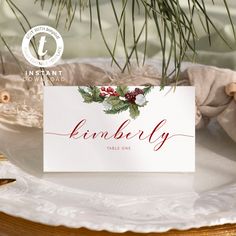 a place card is sitting on a plate with pine cones and holly berries in the center