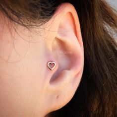 a woman's ear with a small heart shaped piercing on the top of it