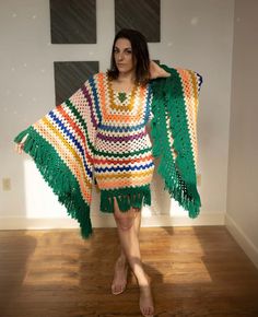 a woman standing in front of a white wall wearing a multicolored crocheted shawl