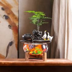 a fish bowl filled with water and plants on top of a wooden table next to a painting