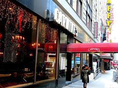 a woman is walking down the sidewalk in front of a store with christmas lights on it