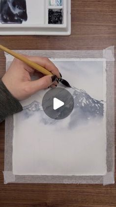 a person is using a pencil to paint a mountain scene