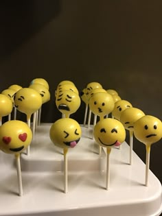 there are many yellow smiley face cake pops on the white stand, all with different expressions