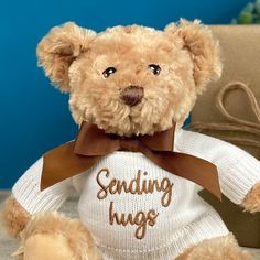 a brown teddy bear wearing a sweater with the words sending hugs on it's chest