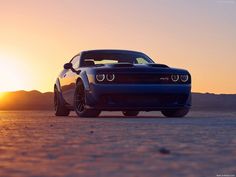 a blue sports car parked in the desert at sunset