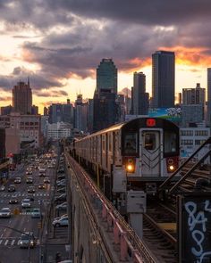 a train traveling through a city next to tall buildings and traffic lights at dusk with the sun setting in the distance