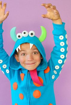 a young boy wearing a monster costume with his hands in the air while standing against a purple background