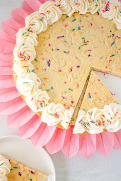 a cake with white frosting and sprinkles on it next to a slice