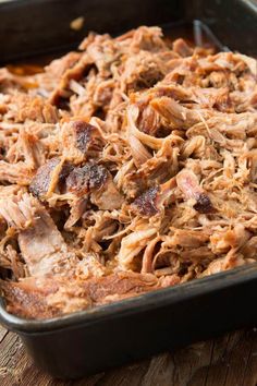 a casserole dish filled with pulled pork in a black pan on top of a wooden table