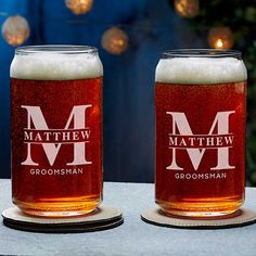 two personalized beer glasses sitting on top of a table with lights in the background