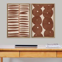 two abstract paintings hang on the wall above a wooden table with a laptop and other items