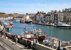 several boats are docked in the water next to some buildings and people walking on the sidewalk