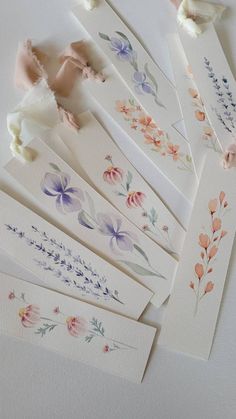 six watercolor flowers and leaves on white paper with pink ribbon tied to them, all lined up in rows