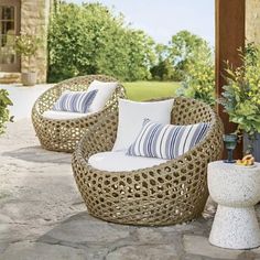 three wicker chairs sitting on top of a stone patio next to potted plants