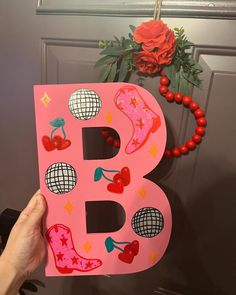 a person holding up a pink letter that says b with decorations on the front door