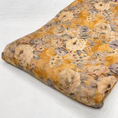 a yellow and brown flowered comforter on a white surface with a red tag hanging from it's side