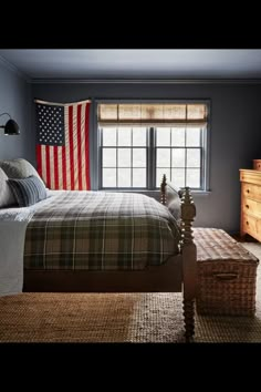 a bedroom with a bed, dresser and an american flag on the window sill