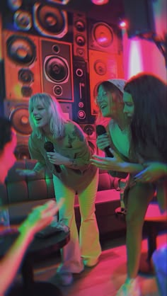 three young women are dancing in front of speakers and microphones while one woman is holding a cell phone