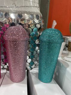 three different colored tumblers sitting on top of a counter next to a mirror and lamp