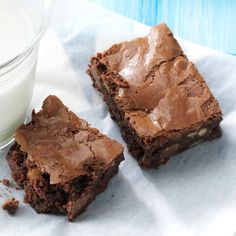 two brownies with chocolate frosting next to a glass of milk on a napkin