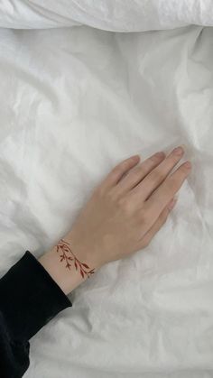 a woman's hand with a tattoo on her left wrist, resting on a white sheet