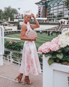 a woman in a pink dress is holding a purse and standing on a race track