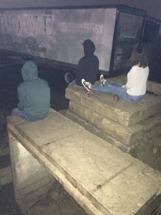 three skateboarders sitting on concrete steps in front of a bus at night time