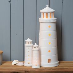 three white lighthouses sitting on top of a wooden table next to a cup and saucer