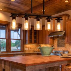 a kitchen with wooden cabinets and lights hanging from the ceiling over the island in front of two windows