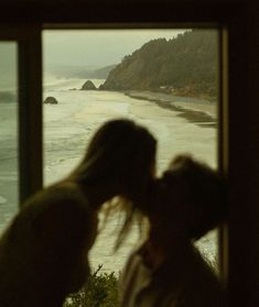 two people standing in front of a window looking out at the ocean