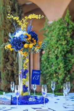 a tall vase filled with yellow and blue flowers sitting on top of a white table cloth