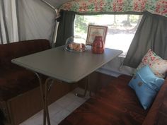 a camper with a table and chairs in front of the window that has curtains on it