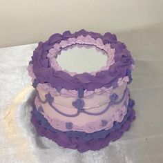 a three tiered cake with purple frosting and flowers on the top is sitting on a table