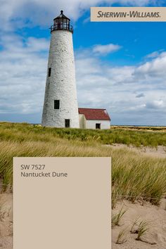 a white lighthouse sitting on top of a grass covered field next to a sandy beach