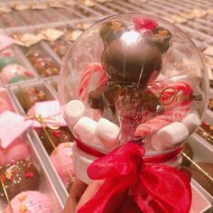 a hand holding a snow globe filled with candies and chocolate covered marshmallows