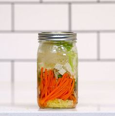 a mason jar filled with carrots, celery and lettuce next to a white tiled wall