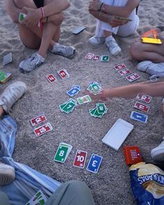 several people sitting on the sand playing with matching cards and games in front of them