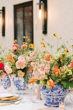 Vibrant table setting with summer florals in blue and white porcelain vases, featuring yellow daisies, peach roses, and orange lilies, set with white dinnerware and gold flatware. Late Summer Weddings, Nature Inspired Wedding, Blue And White Chinoiserie, Wedding Tablescape, Blue Wedding Flowers, Wedding Flowers Summer, Orange Wedding, Brunch Wedding