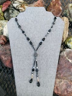 Gunmetal Crystal Hematite Black and Gray Art Deco Elegant Fun Unique Lariat Style Handcrafted Beaded Necklace. Black and Gray Handcrafted Beaded Lariat style Necklace with a single Gunmetal Black and inlaid Crystal Bead as it's Focal point. The 26 inch Beaded Necklace is Dark and Elegant with Hematite Beads of different shapes and sizes that have a Dark Metallic Shine. The Hematite is complimented by Lustrous Gray Mother of Pearl Beads, Black and Gray Network Stone Beads, Gray Aventurine Beads, Beaded Necklace Black, Lariat Style Necklace, Gray Art, Grey Art, Elegant Art, Hematite Beads, Necklace Black, Lariat Necklace, Pressed Glass