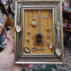 a person holding up a framed photo with many different jewels and spoons in it