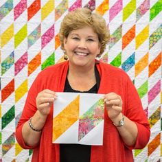 a woman holding up a piece of paper in front of a quilt