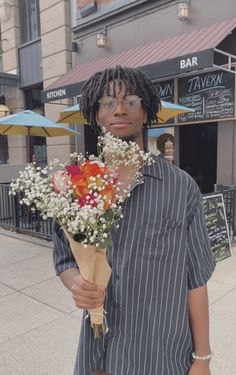 a man holding a bouquet of flowers in front of a building on a city street