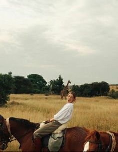 a woman riding on the back of a brown horse next to a giraffe