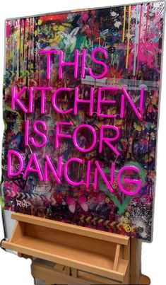 this kitchen is for dancing neon sign in front of an easel with graffiti on it