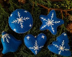 three blue felt ornaments with white snowflakes on them, hanging from a christmas tree